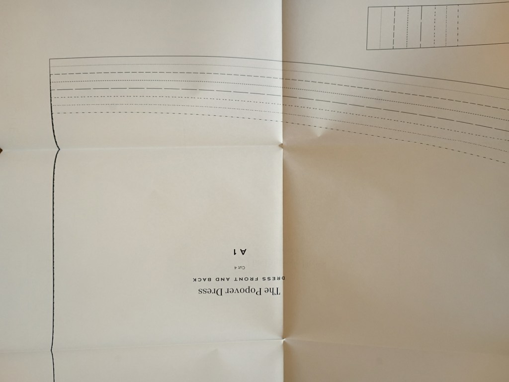 A close-up view of a large white paper sewing pattern sheet from the book, showing different styles of dashed and dotted size lines for the Popover Dress pattern pieces.